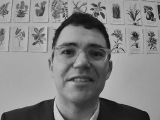 Daniel Powell smiling, pictures of flowers behind him.