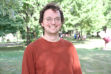 Geoff Meugens smiling with an orange shirt on.
