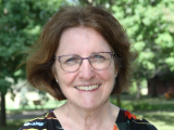 Judith Sabetti smiles with green trees behind her on a sunny day. 